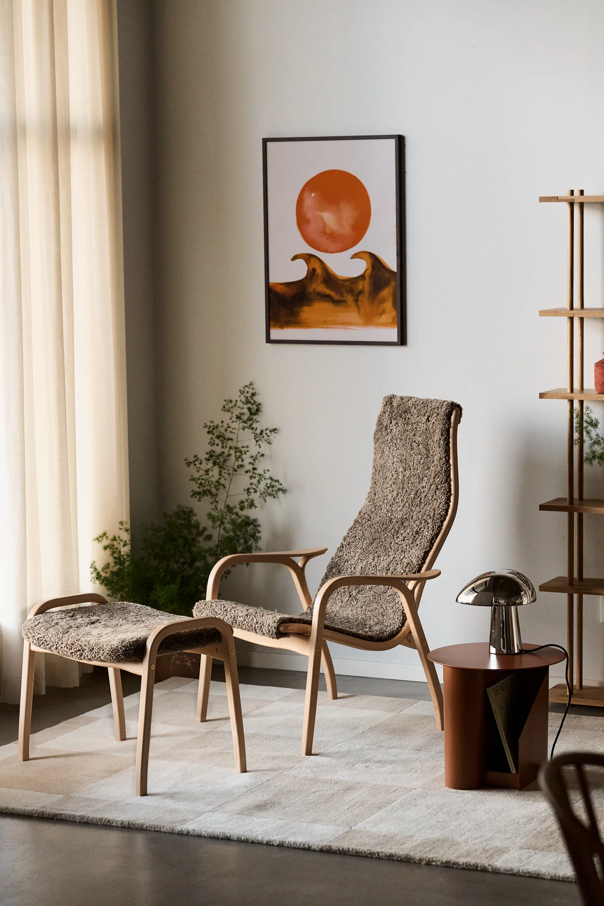 En mysig vardagsrumshörna med ljus träfåtölj, fotpall med brun texturerad klädsel, kromlampa och abstrakt konst.