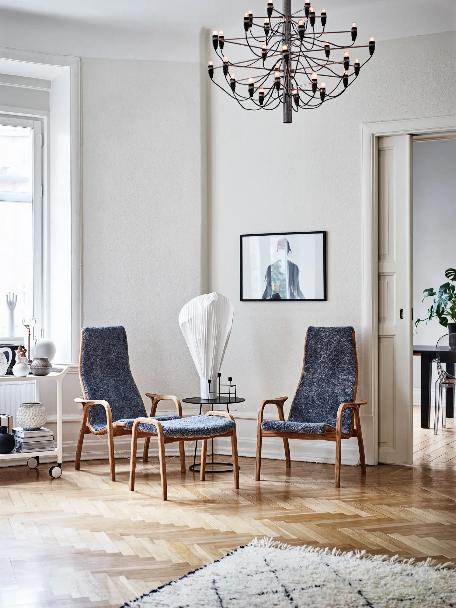 Två Swedese fåtöljer och en fotpall med trästomme och mörkblå klädsel i ett ljust vardagsrum med trägolv.