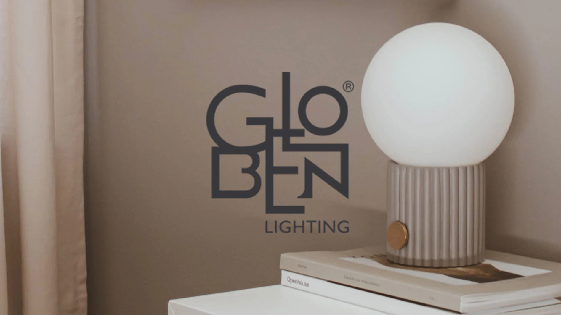 Globen Lighting-logotyp med en vit sfärisk lampa, en grå räfflad bas med en guldfärgad knapp, på böcker bredvid en beige gardin.