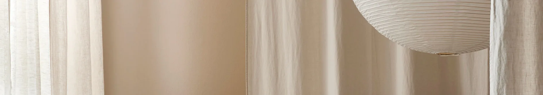 Varmtonad interiör med ljusa skira gardiner, beige vägg och en papperslykta.