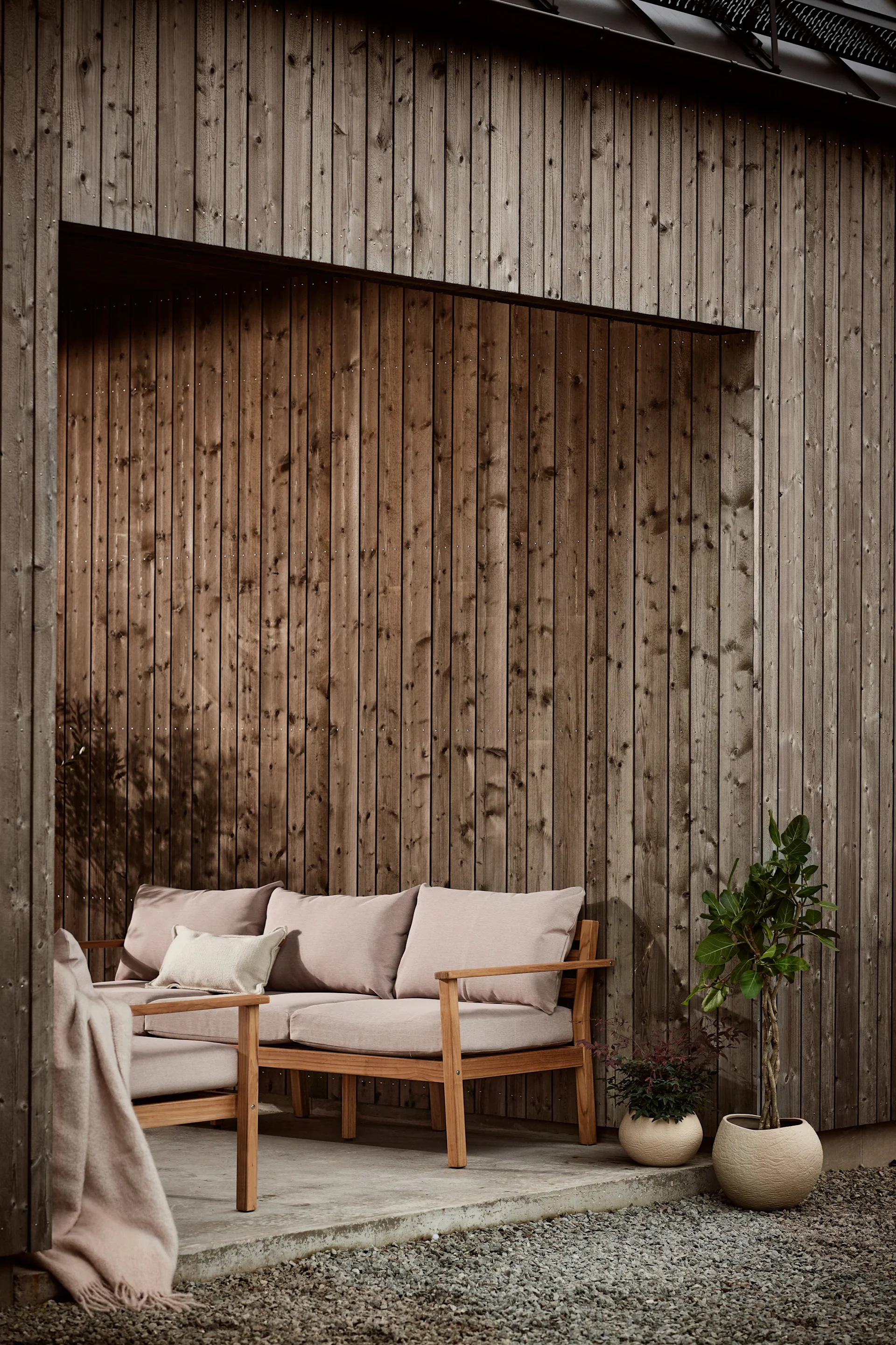 Bland sköna loungemöbler är Stockaryd soffa från 1898 en väl värdig kandidat. Soffan som är tillverkad i teak köps med tillhörande dynor, här stående på uteplats med dynor i beige.