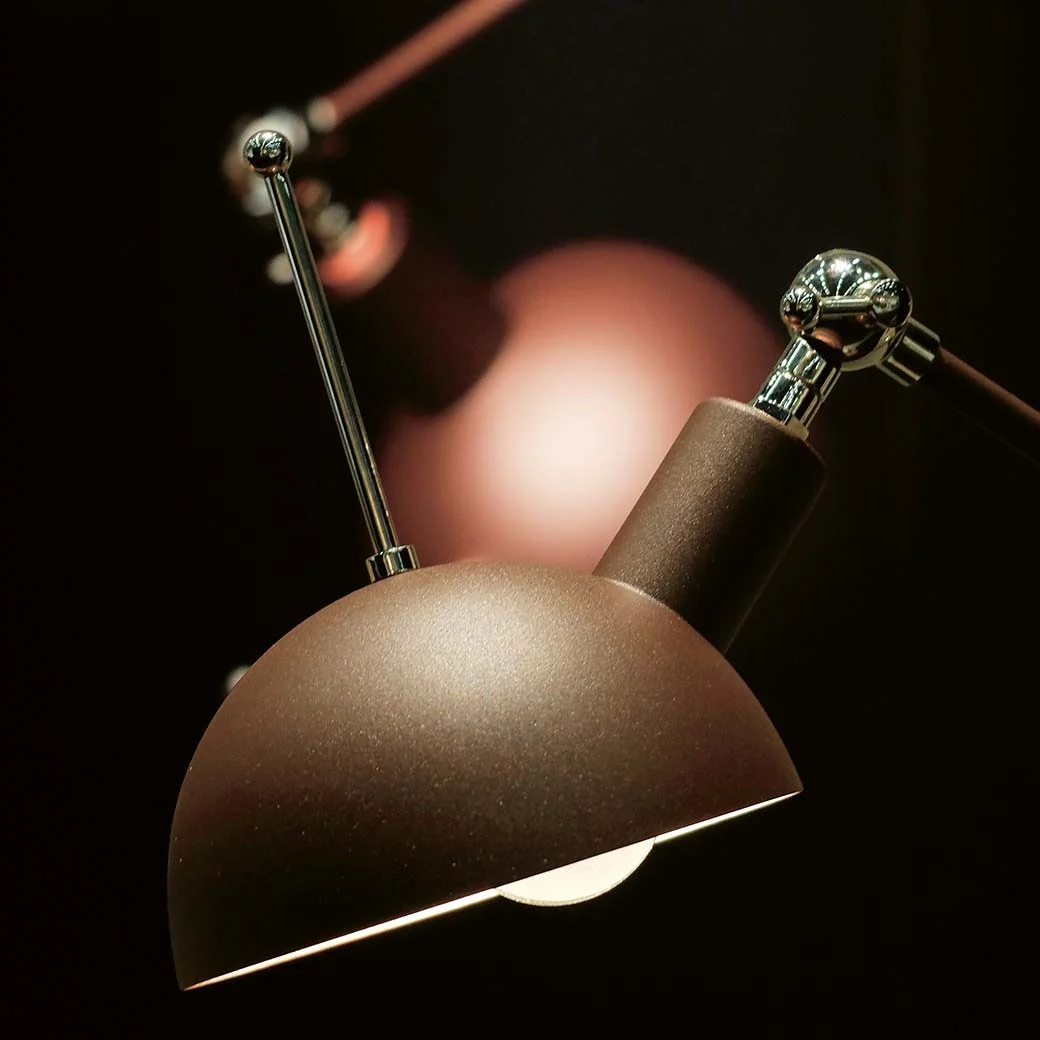 Brun skrivbordslampa med kupolformad skärm och kromdetaljer, ljuset är tänt.
