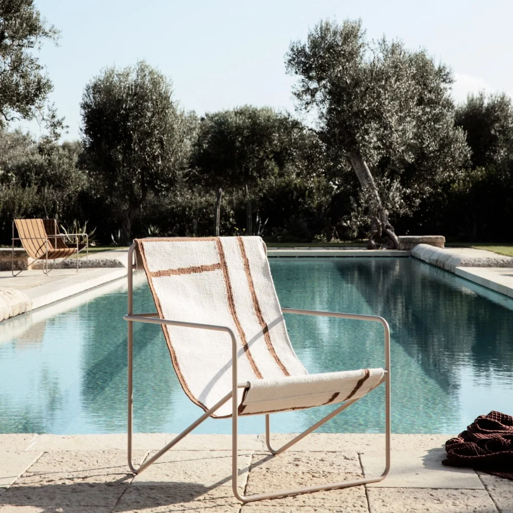 Modern loungestol med randig tygsits vid en pool, med träd i bakgrunden.