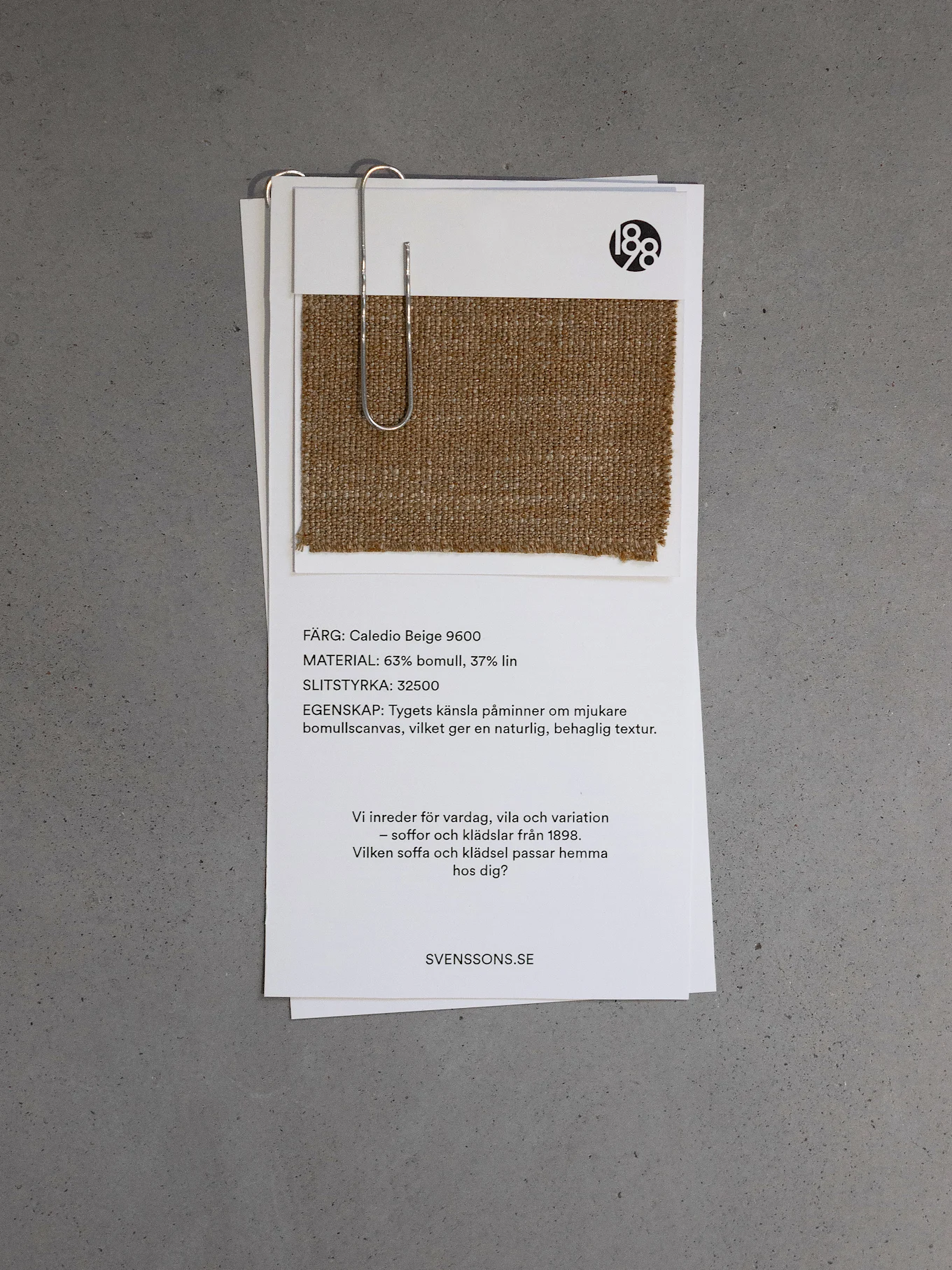 Beigt tygprov med bomulls-/linnetextur, fäst vid ett vitt kort som visar färg, material och slitstyrka.