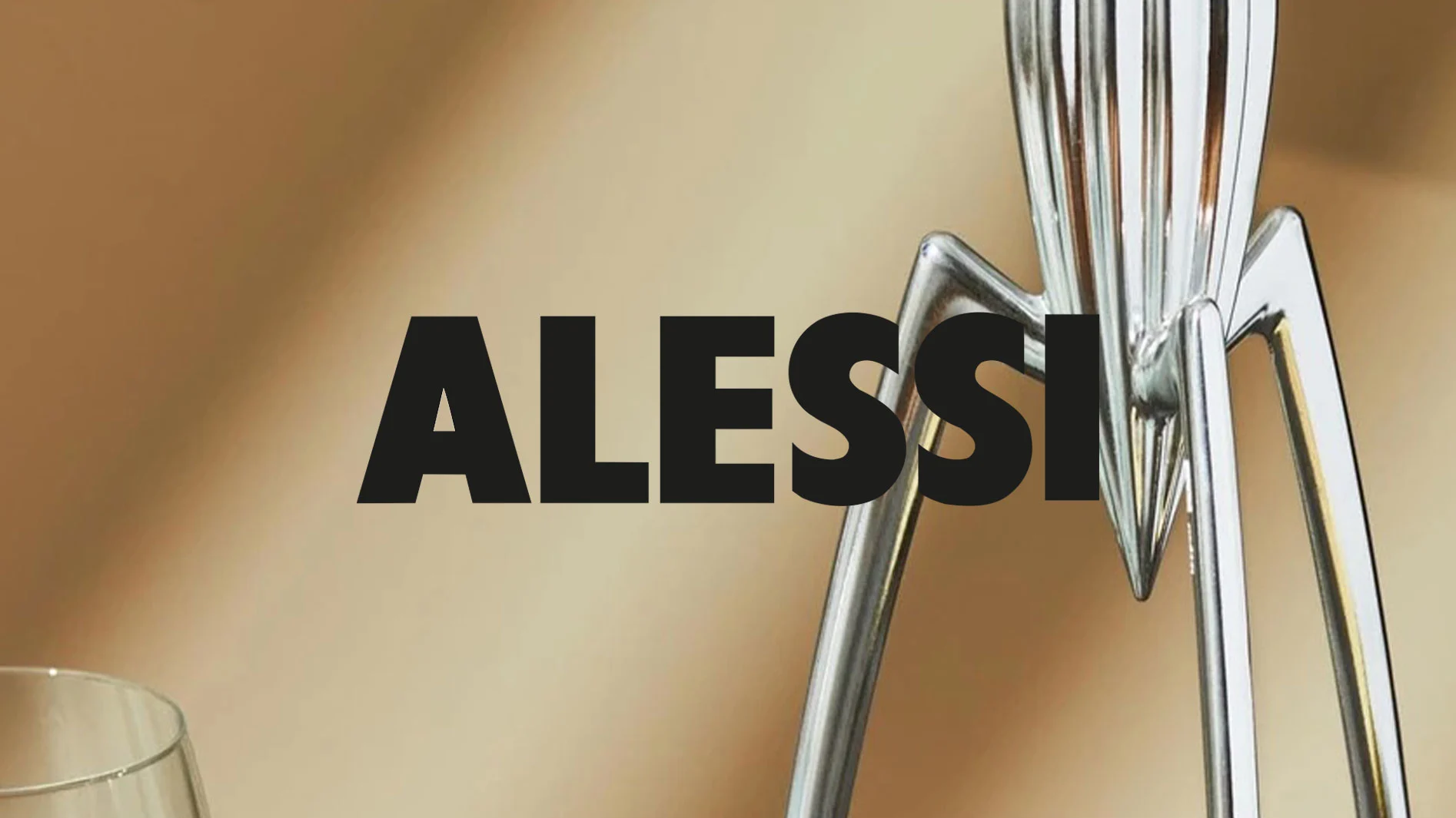 ALESSI-logotyp i svart över brun bakgrund, med en silverfärgad juicepress och ett glas.