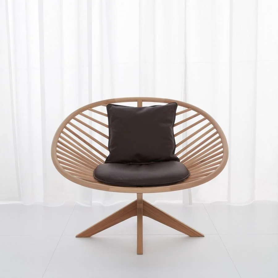 En modern loungestol i ljust trä med ribbad rygg och mörkbruna dynor, på en stativliknande bas mot en vit bakgrund.