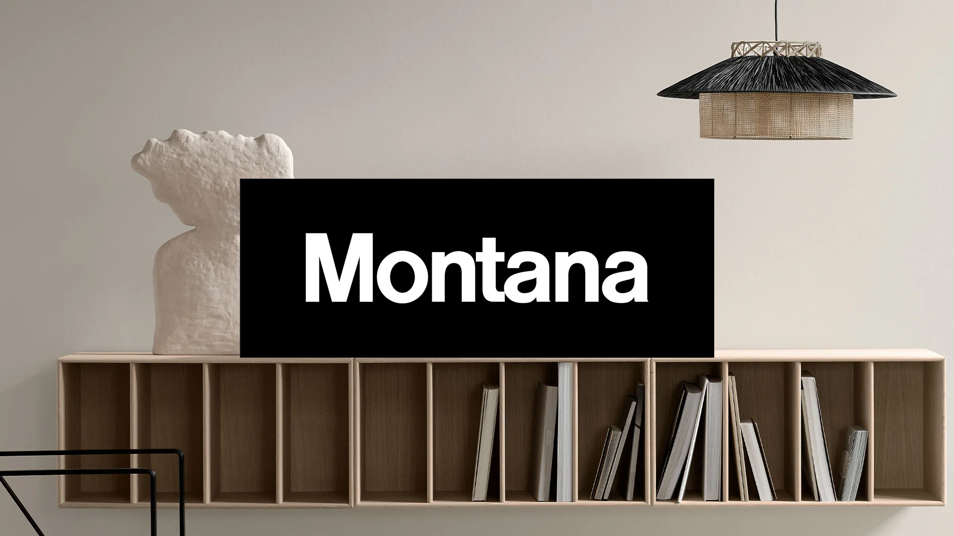 Modernt rum med ljus trähylla, böcker, vit abstrakt skulptur och flätad lampa. Texten «Montana» i ett svart fält.