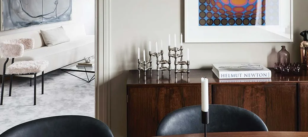 Elegant rum med mörk skänk, silverljusstakar och abstrakt konst. Vit soffa och rosa plyschstol syns.