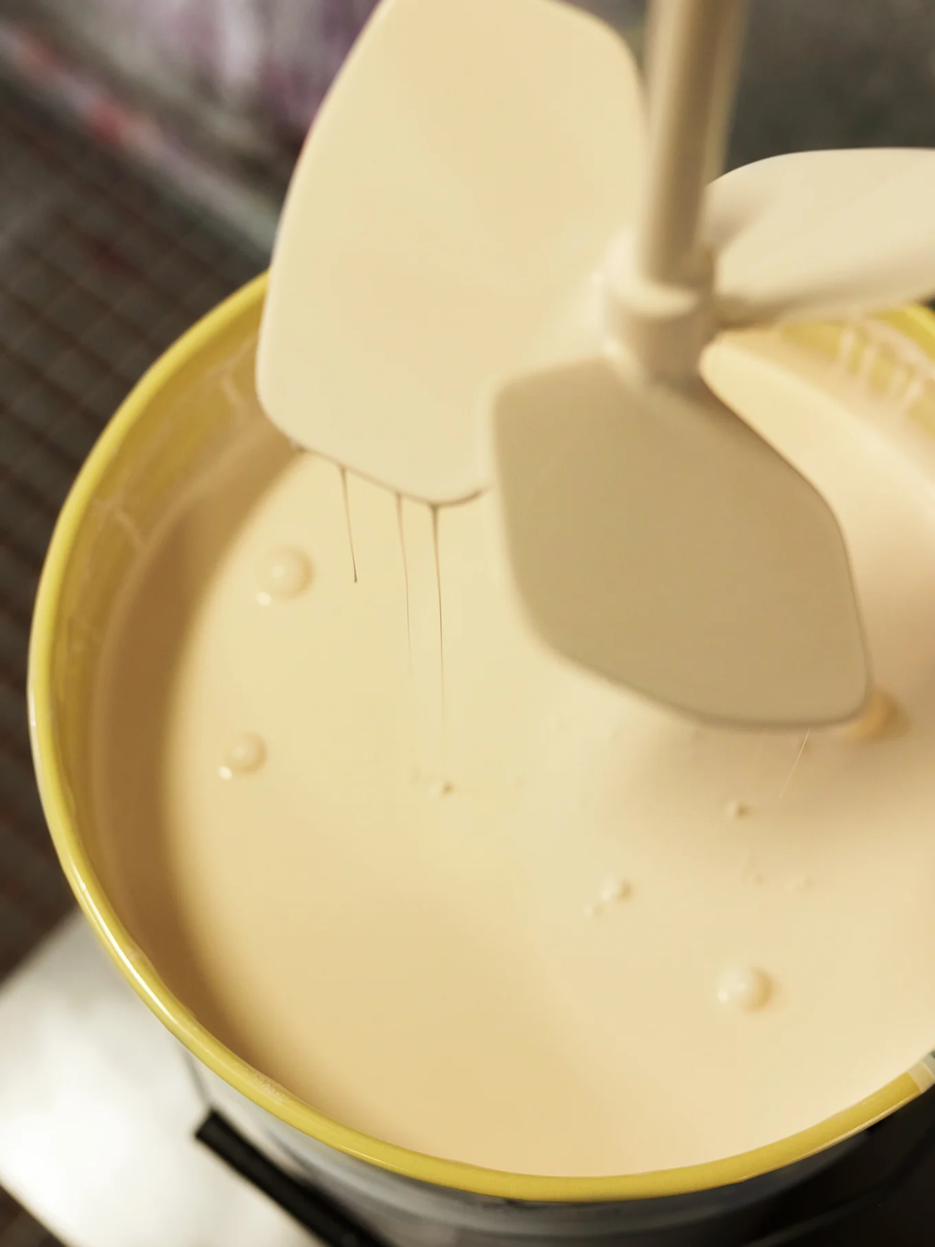Ljus färg i gul hink blandas med vit mixer, med färgdroppar.