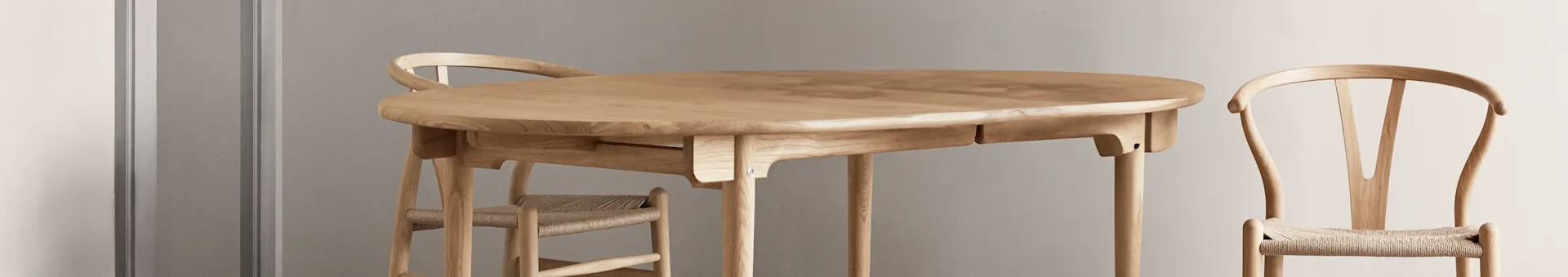 Ljust matbord i trä med oval bordsskiva och två matchande stolar med flätade sitsar.