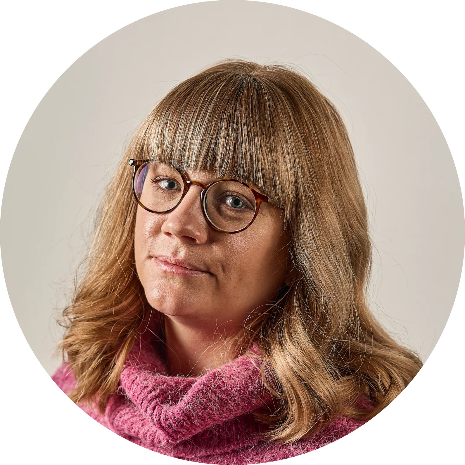 Kvinna med blont hår, lugg och glasögon, iklädd en rosa tröja.