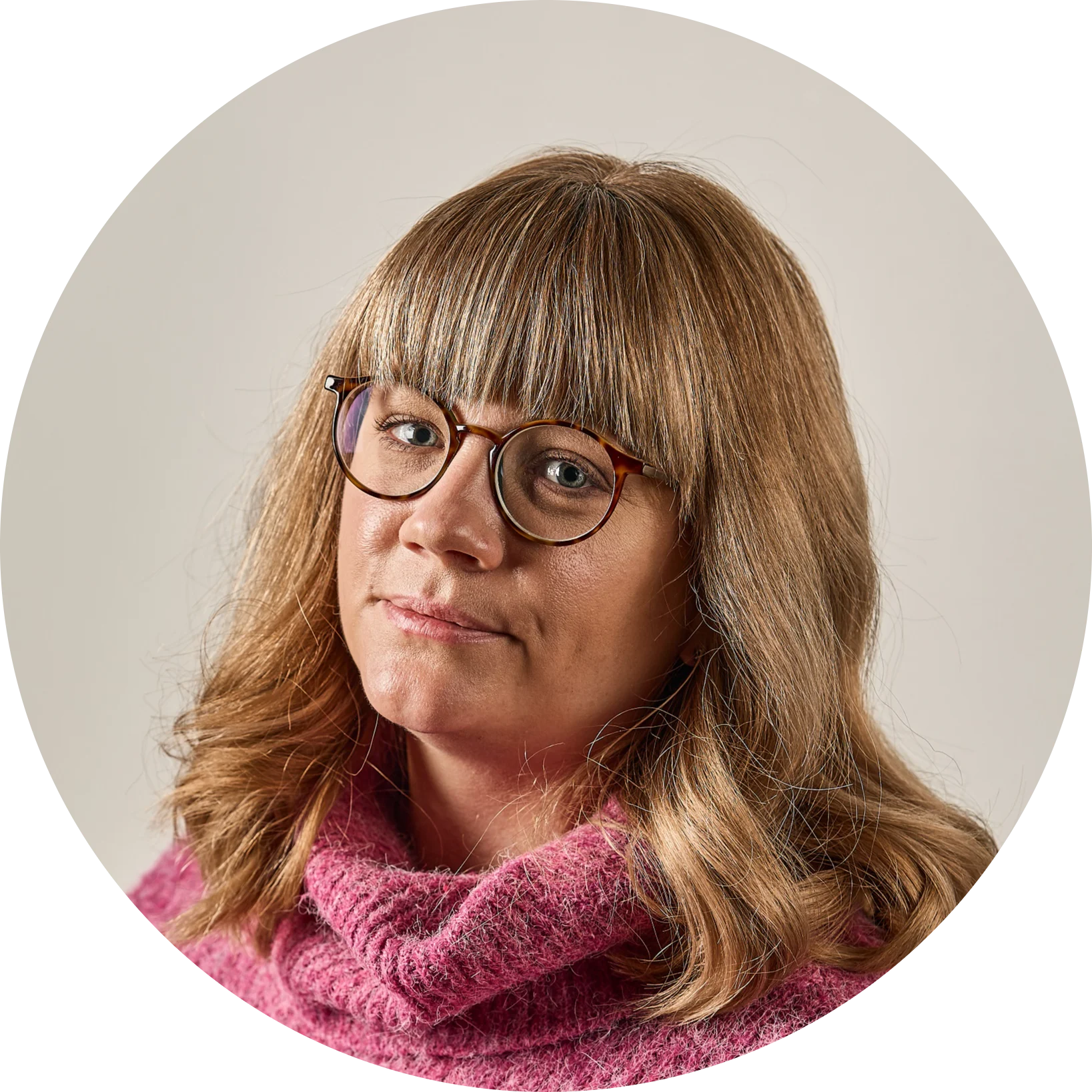 Kvinna med blont hår, lugg och glasögon i en rosa tröja.