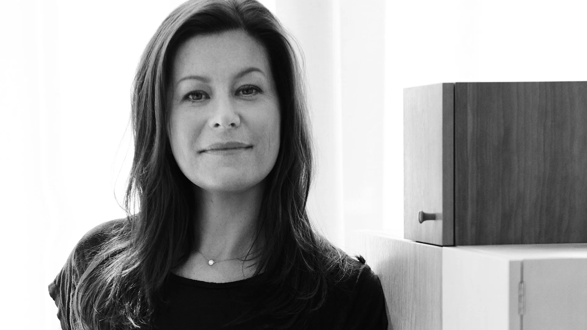 Svartvitt porträtt av en leende kvinna med mörkt hår och halsband.