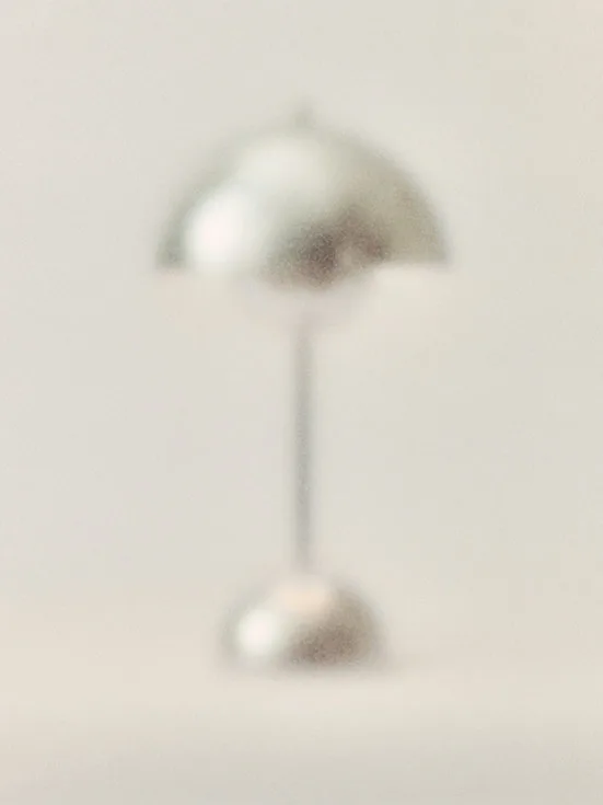 En suddig silverlampa med svampformad skärm och tunn stam på rund fot.