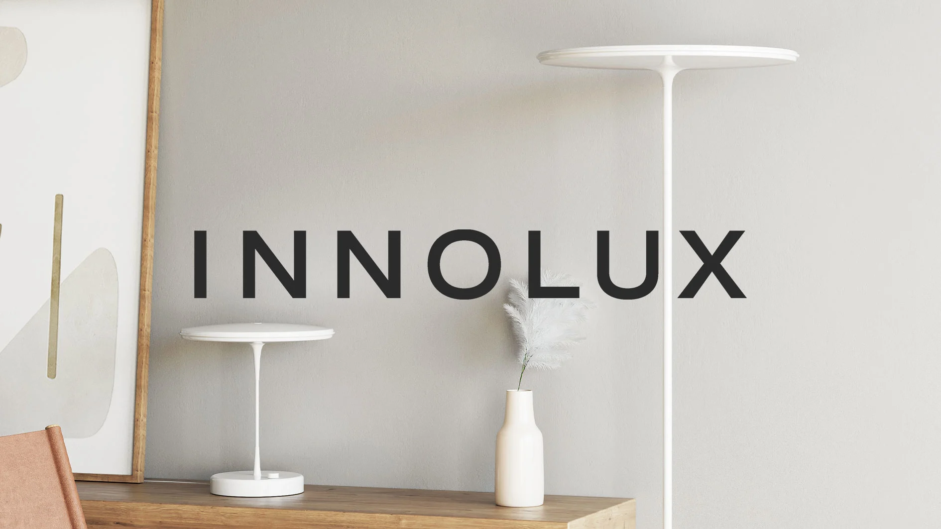 Två vita, moderna lampor (en bordslampa och en golvlampa) med en vas pampasgräs på träyta. Innolux-logotyp.