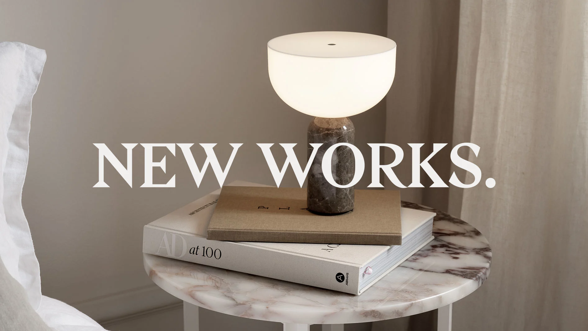 Marmorbord med en lampa med opalglaskupol, böcker, och texten 'NEW WORKS'.