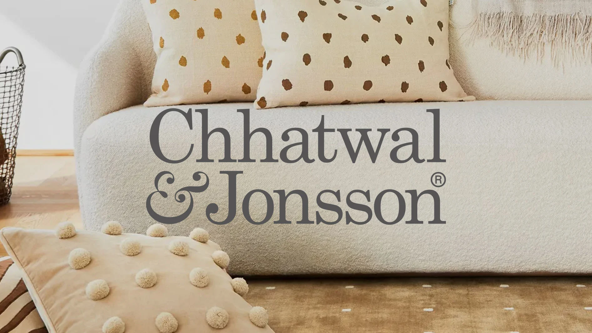 Logotyp för Chhatwal & Jonsson på en ljus soffa med kuddar. En kudde har prickar, en annan har pom-poms.