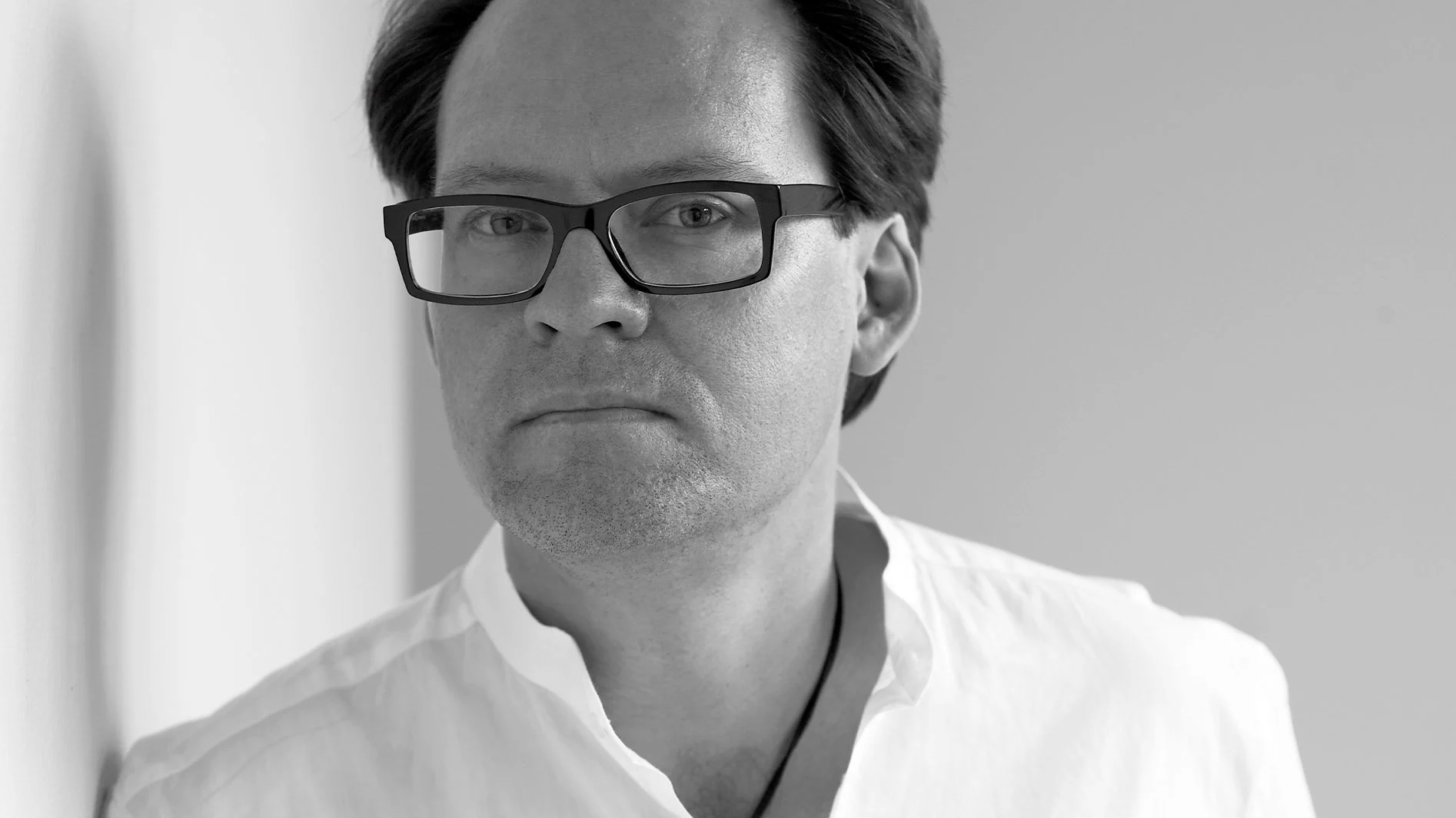 Svartvitt närbild på en man med svarta glasögon och vit skjorta.