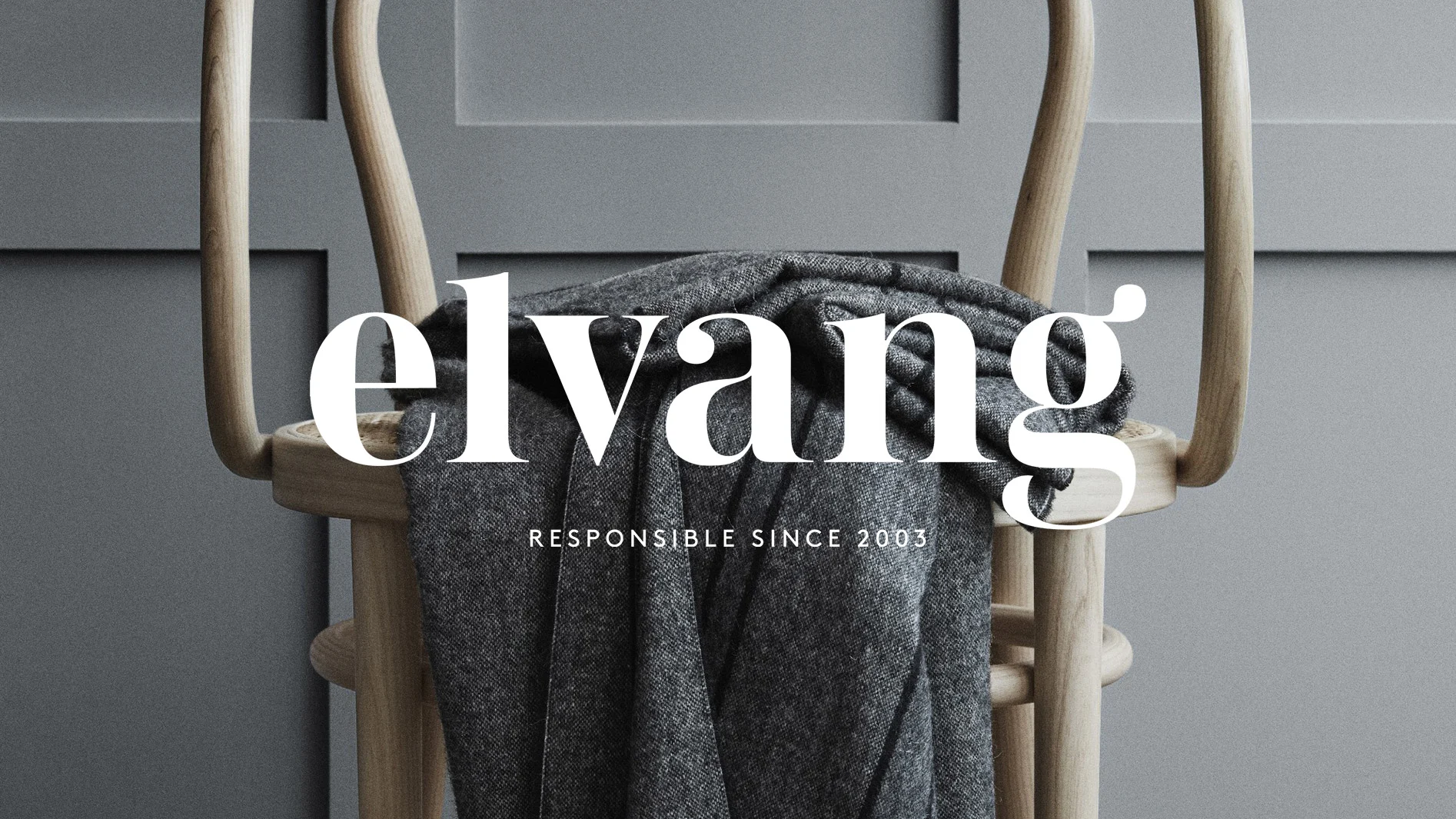 Elvang-logotyp över grå filt på trästol framför en grå panelvägg. Texten "RESPONSIBLE SINCE 2003" är också synlig.
