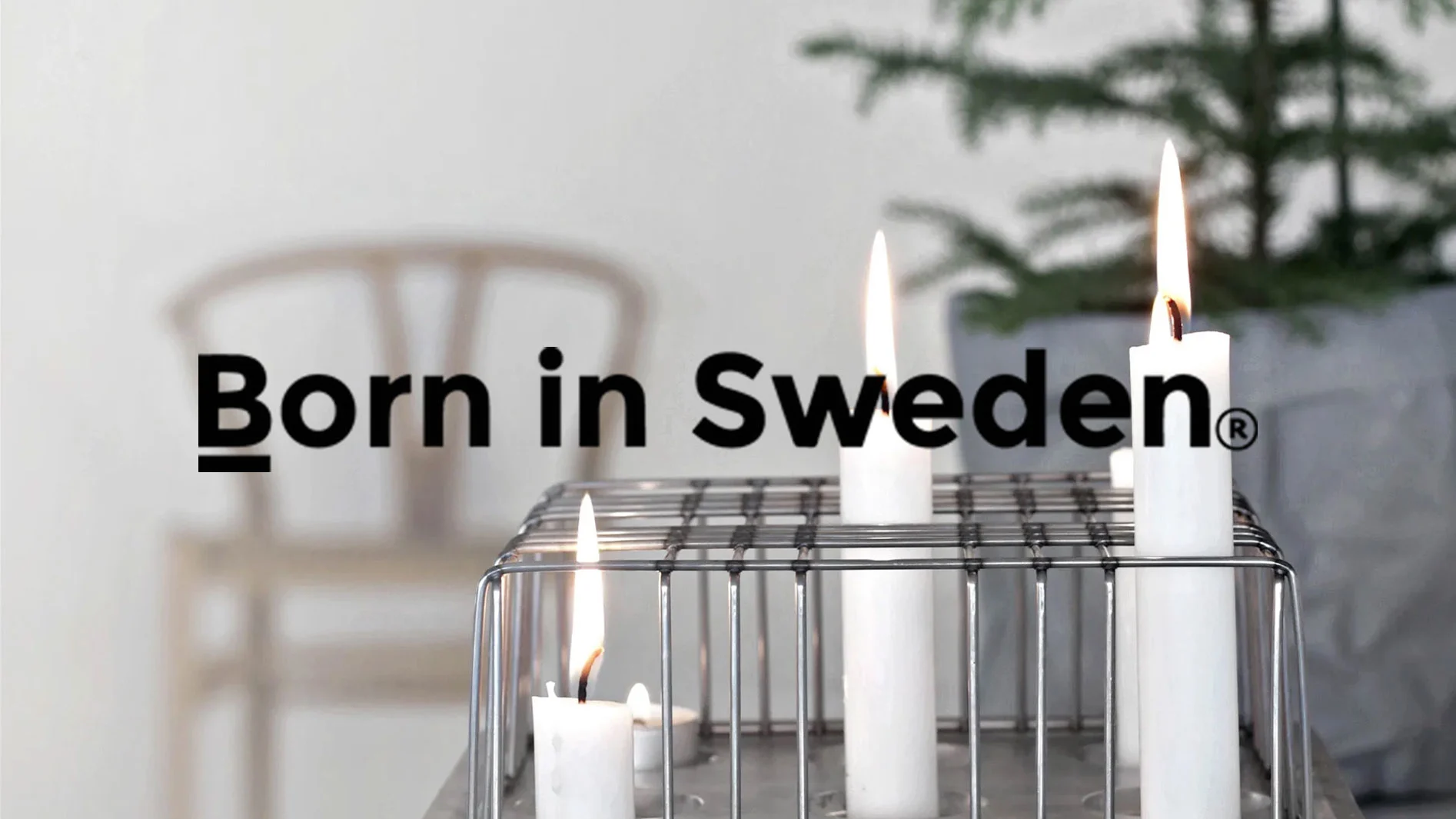 "Born in Sweden"-logotyp över en ljusstake i metall med tre tända vita ljus. I bakgrunden en stol och krukväxt.