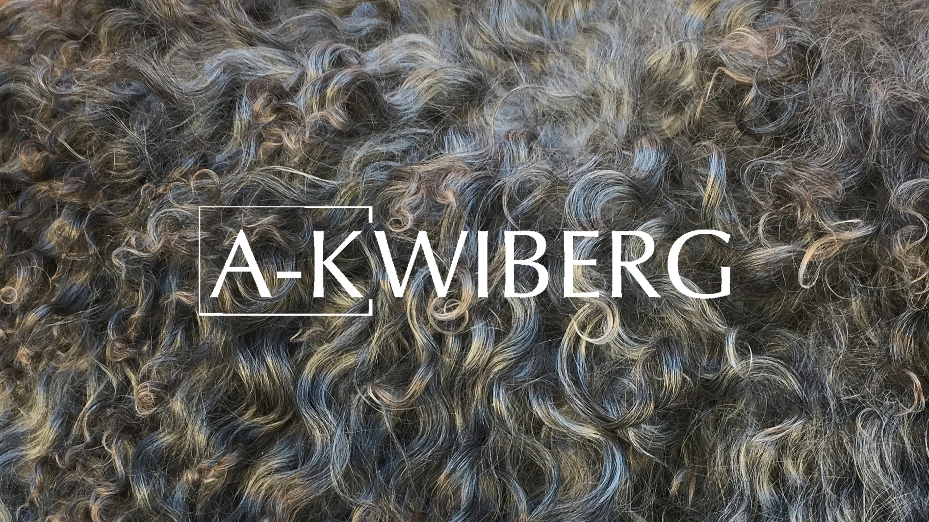 Lockig, mörk ulltextur med grå och bruna nyanser, med namnet A-KWIBERG i vita bokstäver.