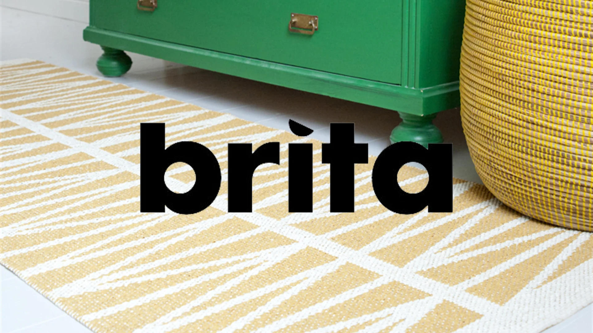 Gul- och vitrandig matta, grön byrå och gul korg på ljust golv. Texten "brita" över bilden.