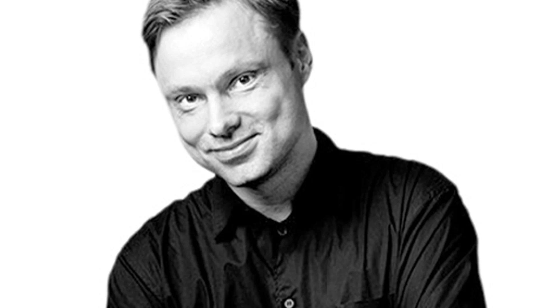 Svartvitt porträtt av en leende man i svart skjorta.