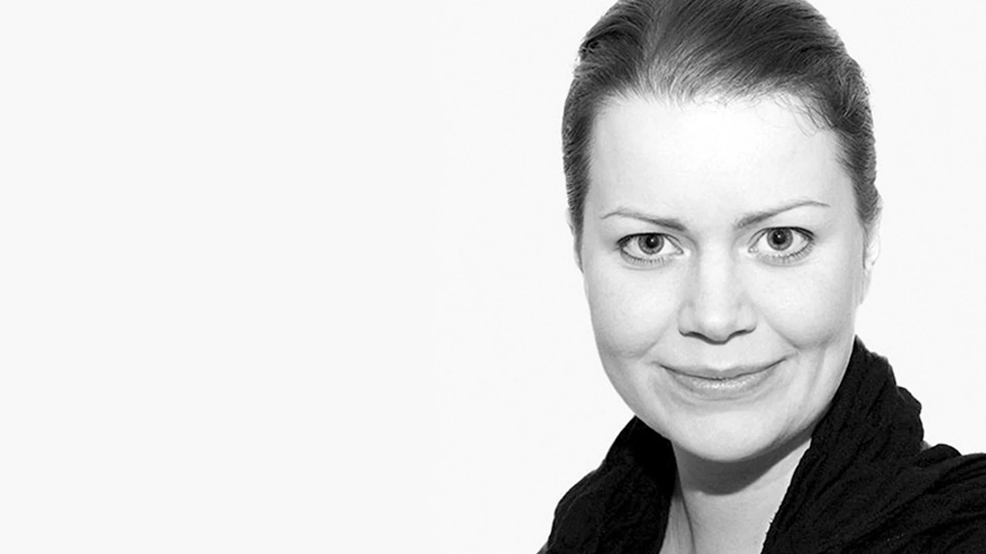 Närbild i svartvitt av en leende kvinna med uppsatt hår som tittar rakt in i kameran.