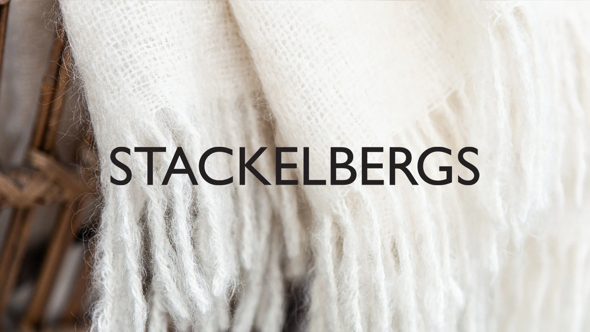 Texten "STACKELBERGS" över en fluffig vit filt med fransar.
