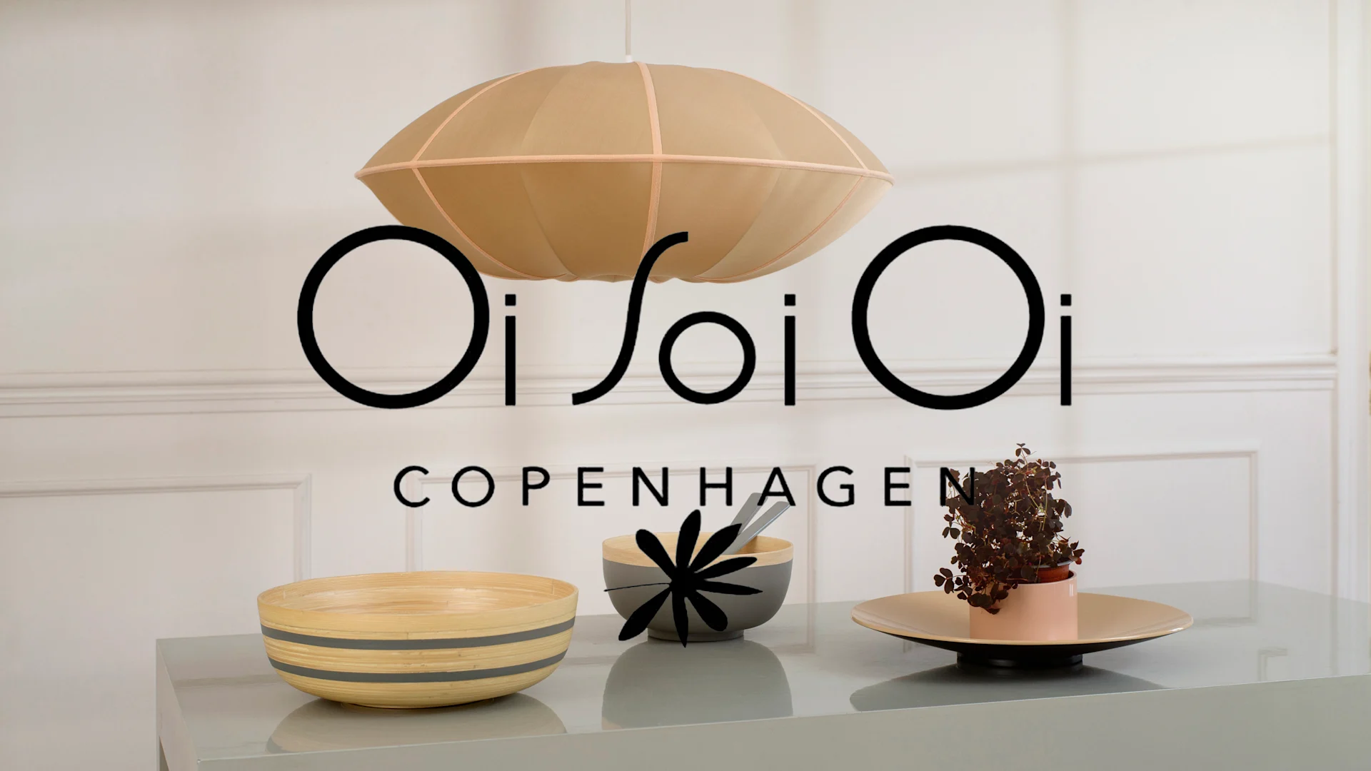 Ljusbrun taklampa, randig bambuskål, grå skål, och krukväxt på bord. Oi Soi Oi Copenhagen.