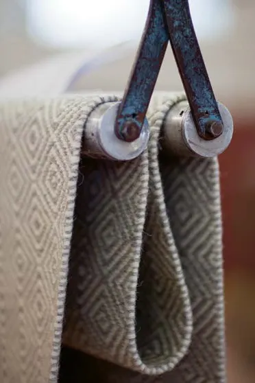 Närbild av ljusgrått vävt tyg med diamantmönster, draperat över två metallrullar.