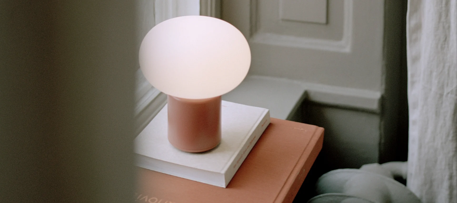 Inred med lampor i fönster som med Karl-Johan portabel bordslampa från New Works, här i färgen earth red placerad på böcker i en djup fönsternisch.