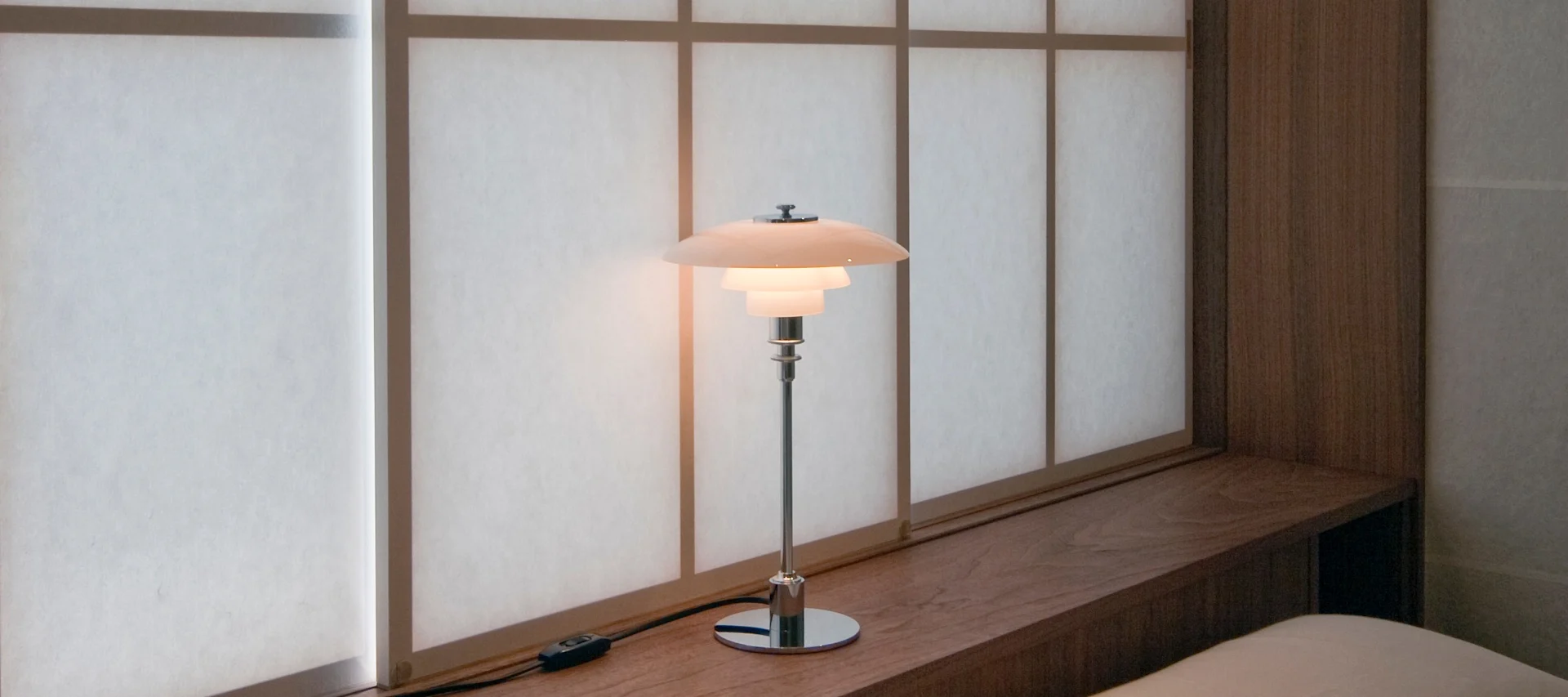 Inred med lampor i fönster som med Karl-Johan portabel bordslampa från New Works, här i färgen earth red placerad på böcker i en djup fönsternisch. 